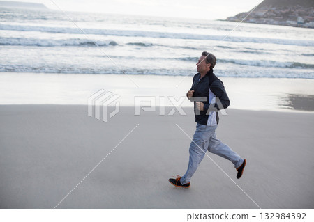 Man jogging along wet sand at shoreline wearing athletic jacket and running shoes, copy space Man jogging along wet sand at shoreline wearing athletic jacket and running shoes, copy space 132984392