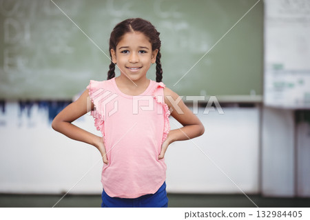 Preteen girl standing with hands on hips and smiling in classroom with chalkboard equations 132984405