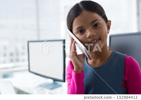 Asian girl smiling while holding smartphone against ear in home office with monitors, copy space 132984412