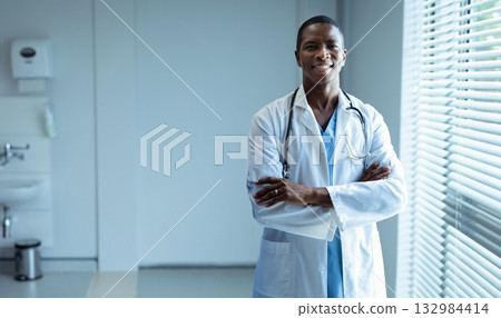 African American doctor standing by window in clinic wearing lab coat with stethoscope, copy space African American doctor standing by window in clinic wearing lab coat with stethoscope, copy space 132984414