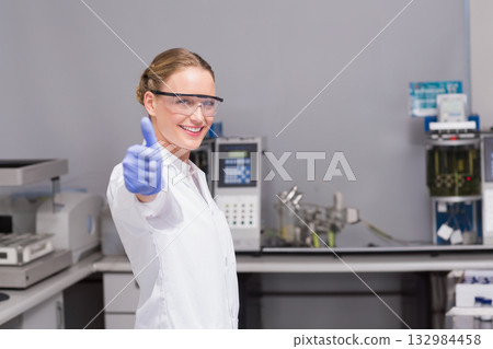 Female scientist giving thumbs up in lab with instruments wearing lab coat and goggles, copy space Female scientist giving thumbs up in lab with instruments wearing lab coat and goggles, copy space 132984458