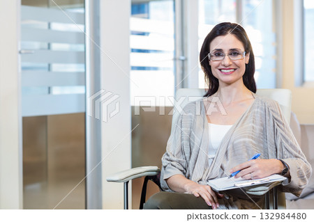 Female office worker wearing cardigan smiling and holding clipboard and pen in office, copy space Female office worker wearing cardigan smiling and holding clipboard and pen in office, copy space 132984480