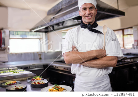 Male chef holding spoon under arm in commercial kitchen displaying salads and pasta, copy space 132984491