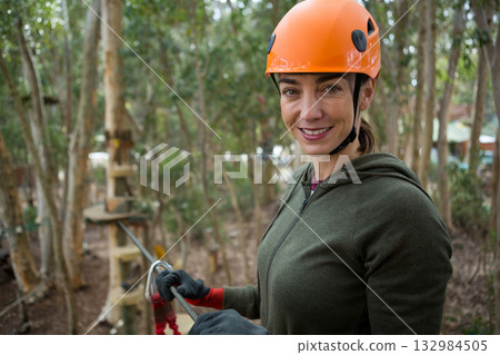 Female wearing orange helmet gripping steel cable on platform of outdoor rope course, copy space Female wearing orange helmet gripping steel cable on platform of outdoor rope course, copy space 132984505