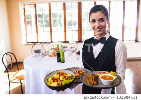 Female server holding trays laden with salad soup bread appetizers in banquet hall, copy space Female server holding trays laden with salad soup bread appetizers in banquet hall, copy space 132984511