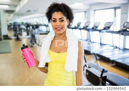 African American woman holding pink water bottle near treadmills and mirror wall in cardio area 132984542