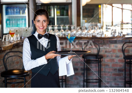 Female server holding blue cocktail on tray with lemon slice in brick bar with refrigerated display 132984548