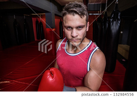 Male boxer practicing punches on heavy bag in martial arts gym wearing red gloves and top 132984556