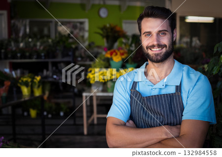 Male florist standing in flower shop wearing striped apron by buckets of flowers, copy space 132984558