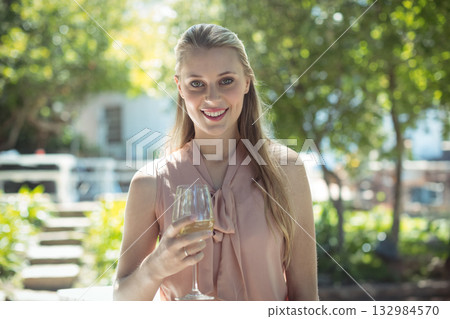 Woman smiling while holding wine glass on sunlit terrace wearing peach blouse with bow Woman smiling while holding wine glass on sunlit terrace wearing peach blouse with bow 132984570