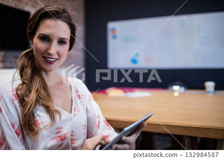 Woman in mid twenties holding tablet at conference table with coffee cup and whiteboard, copy space Woman in mid twenties holding tablet at conference table with coffee cup and whiteboard, copy space 132984587