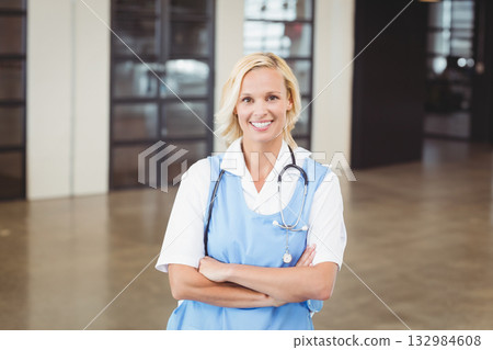 Woman in her thirties wearing light blue scrubs standing in medical lobby holding stethoscope badge 132984608