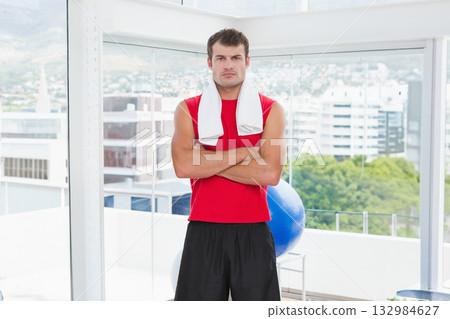 African American man standing next to large windows in fitness studio with towel and exercise ball 132984627