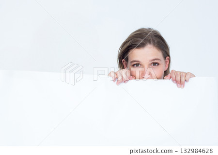 Woman peeking over large blank white panel in studio, framing minimalist backdrop 132984628