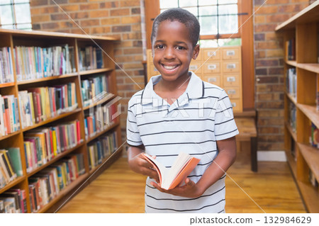African American boy holding open book, smiling and standing near library bench and card catalog 132984629