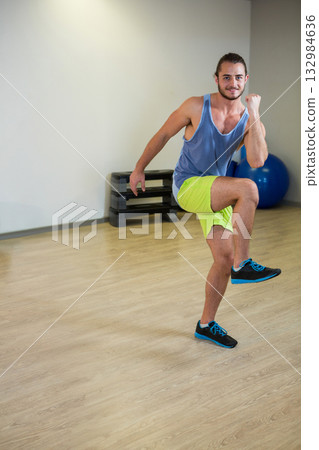 Man in tank and shorts performing high-knee exercise in gym with step platforms, copy space 132984636
