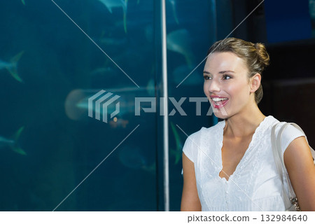 Adult woman standing before aquarium tank with shoulder bag, gazing at fish silhouettes, copy space Adult woman standing before aquarium tank with shoulder bag, gazing at fish silhouettes, copy space 132984640