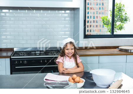 Female child wearing white chef hat whisking eggs at home kitchen counter next to gas range 132984645