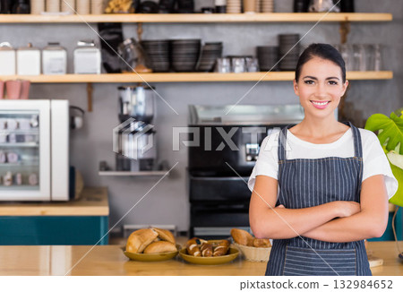 Female barista standing behind wooden counter displaying pastry trays and rolls at cafe, copy space Female barista standing behind wooden counter displaying pastry trays and rolls at cafe, copy space 132984652