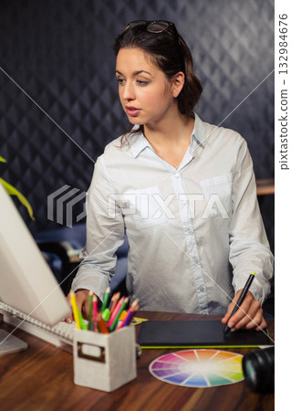 Woman working at wooden desk in design studio using stylus on graphics tablet with color wheel 132984676