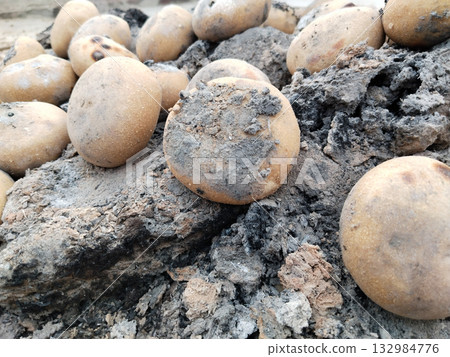 Round wheat flour balls being roasted on residual ashes of burnt cow dung cakes in traditional Indian village method, showing post-fire slow cooking technique used for preparing litti Round wheat flour balls being roasted on residual ashes of burnt cow dung cakes in traditional Indian village method, showing post-fire slow cooking technique used for preparing litti 132984776