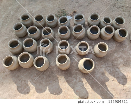 Multiple raw clay pots sun-drying outdoors in rural pottery workshop, showcasing traditional handmade earthenware in natural sunlight as part of village craftsmanship process Multiple raw clay pots sun-drying outdoors in rural pottery workshop, showcasing traditional handmade earthenware in natural sunlight as part of village craftsmanship process 132984811