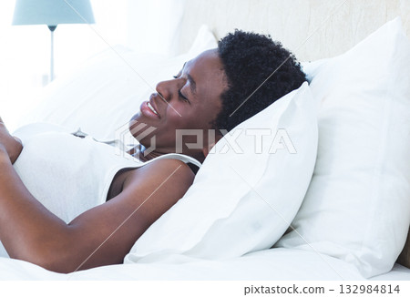 African American mid adult woman wearing tank top reclining on bed beside lamp with muted shade African American mid adult woman wearing tank top reclining on bed beside lamp with muted shade 132984814