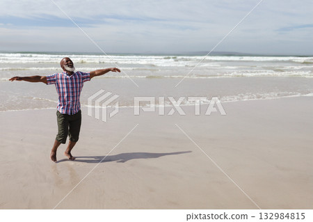 African American man stretching arms on beach wearing rolled-up pants barefoot with waves rolling African American man stretching arms on beach wearing rolled-up pants barefoot with waves rolling 132984815