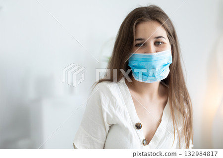 Woman wearing blue surgical mask and white blouse standing toward camera in lit bedroom Woman wearing blue surgical mask and white blouse standing toward camera in lit bedroom 132984817