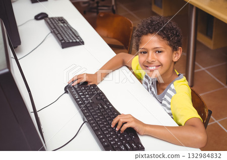 African American boy smiling and sitting at school computer lab desk using monitor, copy space African American boy smiling and sitting at school computer lab desk using monitor, copy space 132984832