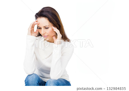 Woman holding temples while tilting head down seated against white background in studio 132984835