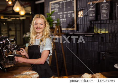 Smiling female barista using portafilter to fill coffee cup on espresso machine at shop counter 132984865