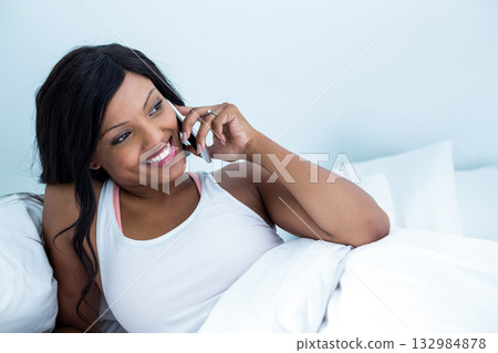 African American woman reclining in bed in bedroom holding smartphone and displaying ring on finger African American woman reclining in bed in bedroom holding smartphone and displaying ring on finger 132984878