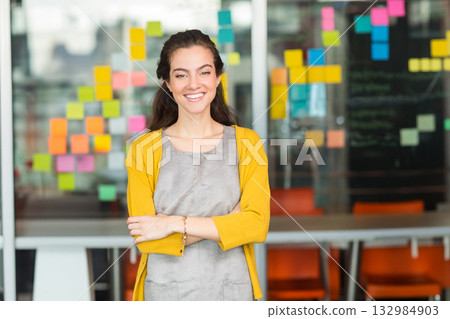 Female professional standing smiling by glass wall with sticky notes beside meeting table in office 132984903