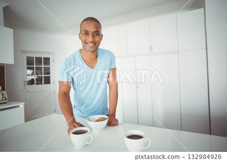 African American man leaning on countertop in modern kitchen, smiling at camera with cereal bowl African American man leaning on countertop in modern kitchen, smiling at camera with cereal bowl 132984926