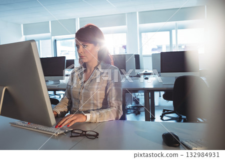 Female professional using keyboard and mouse at desk in computer lab with monitor and eyeglasses 132984931