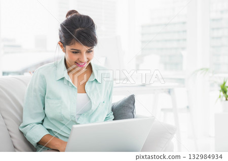 Asian woman typing on laptop on sofa with decorative cushion in modern living room 132984934