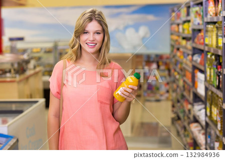 Woman standing in supermarket aisle holding orange juice bottle and wearing coral short sleeve top Woman standing in supermarket aisle holding orange juice bottle and wearing coral short sleeve top 132984936