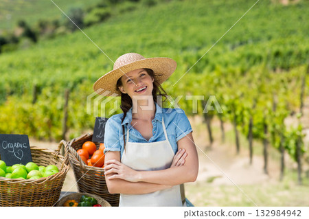 Female vendor standing at vineyard stand wearing apron displaying produce and sign reading Organic 132984942