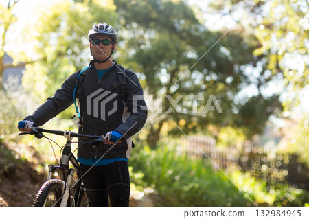 Male cyclist pausing on forest trail with mountain bike wearing helmet sunglasses hydration pack 132984945