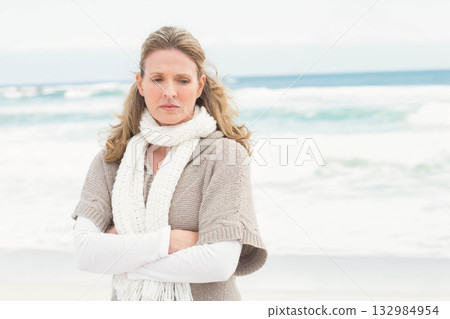 Woman gazing downward on sandy shoreline wearing knit poncho and scarf beside ocean waves Woman gazing downward on sandy shoreline wearing knit poncho and scarf beside ocean waves 132984954
