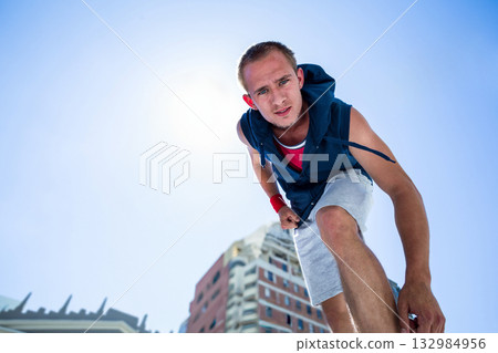 Leaning toward camera, man wearing hoodie, tank top, shorts, sweatband on urban street, copy space Leaning toward camera, man wearing hoodie, tank top, shorts, sweatband on urban street, copy space 132984956