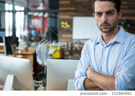 Adult male in blue shirt standing with arms crossed by whiteboard in open-plan office, copy space 132984981