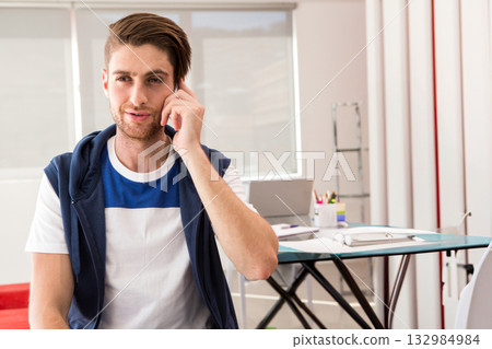Man talking on smartphone at home office desk with laptop, papers and colored pencils, copy space 132984984