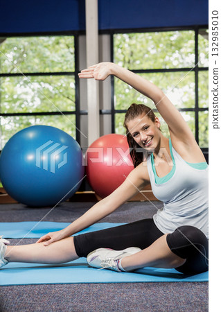 Woman in sportswear stretching sideways on gym mat beside blue and red stability balls, copy space Woman in sportswear stretching sideways on gym mat beside blue and red stability balls, copy space 132985010