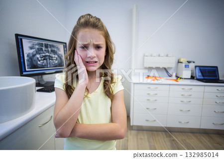 Preteen girl patient pressing hand against cheek in dental exam room with x-ray monitor and tools Preteen girl patient pressing hand against cheek in dental exam room with x-ray monitor and tools 132985014