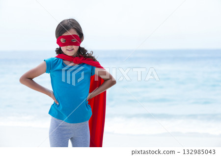 Girl standing on sandy shoreline wearing red superhero cape and eye mask, copy space Girl standing on sandy shoreline wearing red superhero cape and eye mask, copy space 132985043