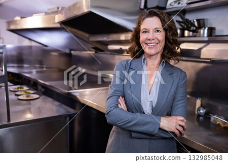 Senior woman supervising salad plating in restaurant kitchen with steel counters, copy space 132985048