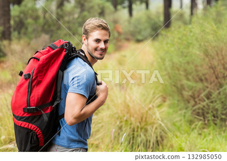 Male hiker hiking on pine forest trail smiling, carrying red backpack with black straps, copy space Male hiker hiking on pine forest trail smiling, carrying red backpack with black straps, copy space 132985050