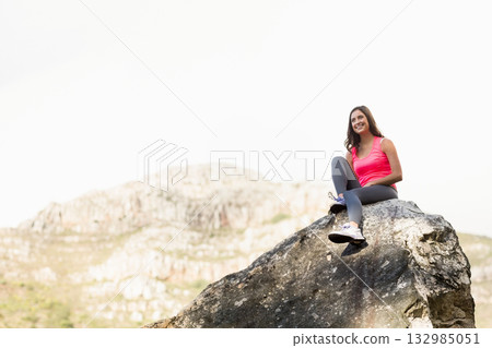 Woman sitting on boulder in mountains wearing athletic shoes, leggings, pink tank top, copy space Woman sitting on boulder in mountains wearing athletic shoes, leggings, pink tank top, copy space 132985051